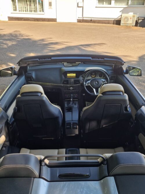 Overhead view of the 2012 Mercedes-Benz E-Class E250 Cabriolet interior with the roof down, showing the dashboard, beige leather seats, and AMG styling
