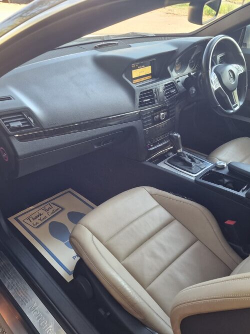 Interior view of a 2012 Mercedes-Benz E-Class Cabriolet showcasing cream leather seats, multifunction steering wheel, and a premium centre console with automatic transmission